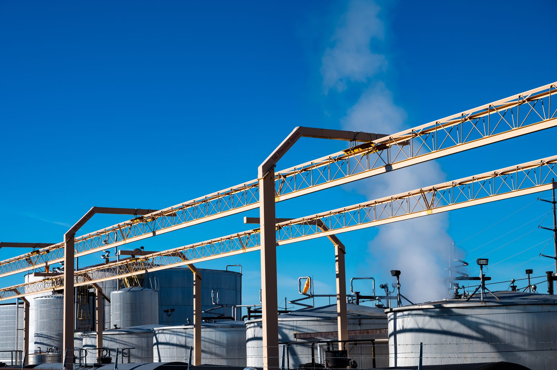 Wide view of an industrial plant with smoke rising from storage tanks against a clear blue sky. — rafineria ropy naftowej