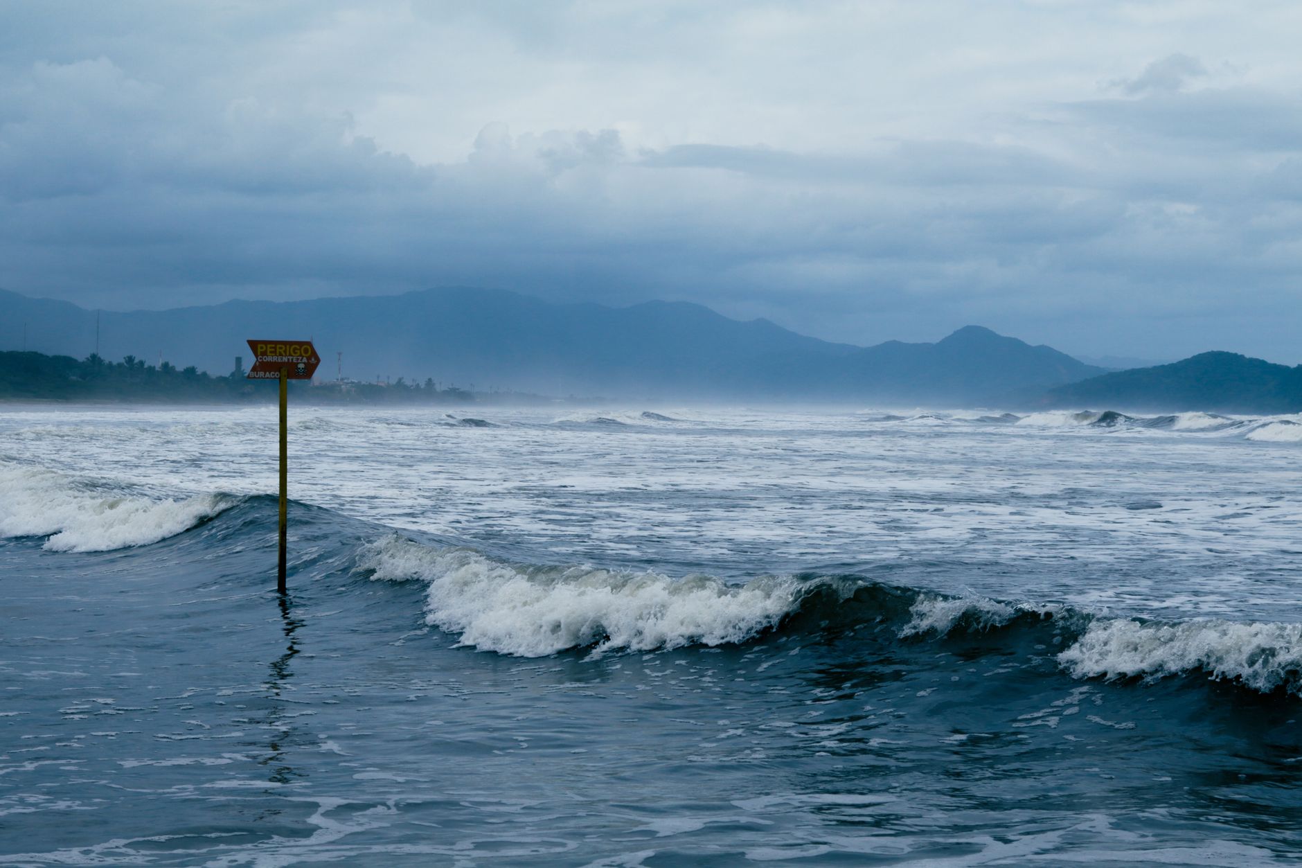 Cloudy coastal scene with warning sign and waves crashing against the shore, conveying sea caution. — trzęsienie ziemi w Panamie
