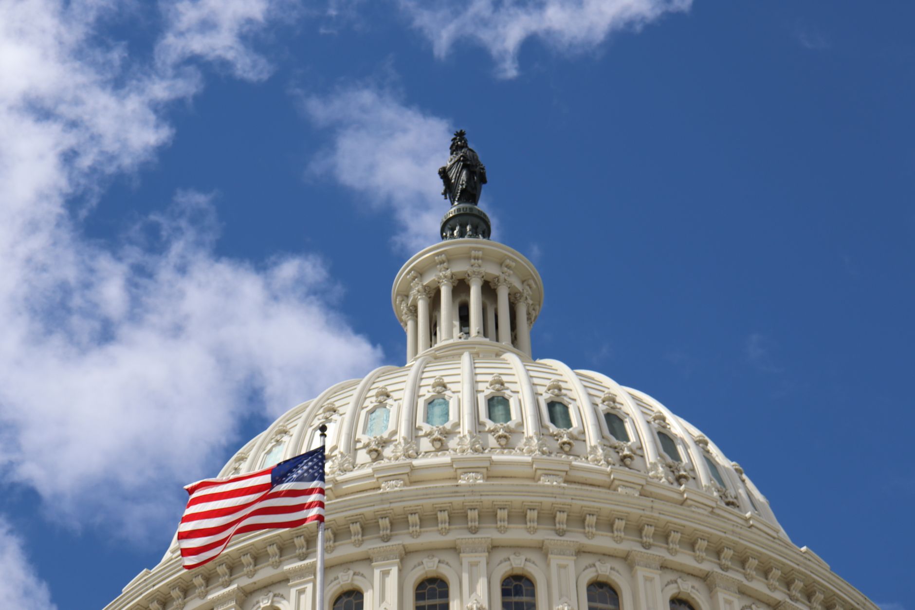 Capture of the U.S. Capitol dome with an American flag waving against a blue sky in Washington, D.C. — Kongres Polonii Amerykańskiej