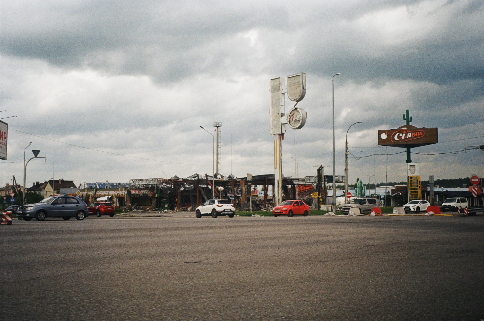 Urban street view in Kyiv showing cars, cloudy sky, and damaged structures. — wojna w Ukrainie