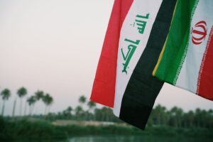 Iraqi and Iranian flags waving with palm trees in the background, Karbala, Iraq. — USA i Iran przed wyborami