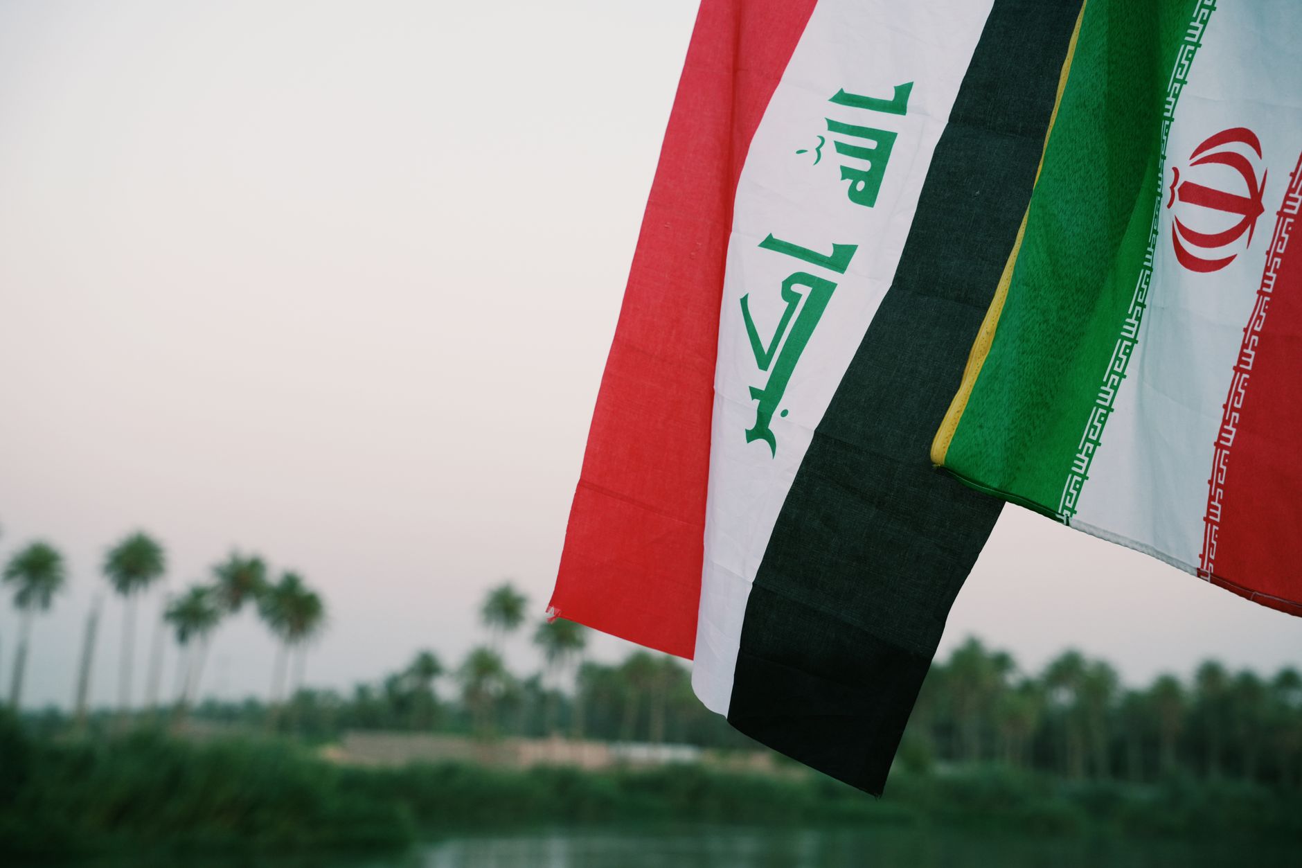 Iraqi and Iranian flags waving with palm trees in the background, Karbala, Iraq. — USA i Iran przed wyborami