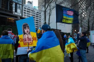 A group of protesters holding signs and Ukrainian flags in an urban setting. — presja USA na Ukrainę