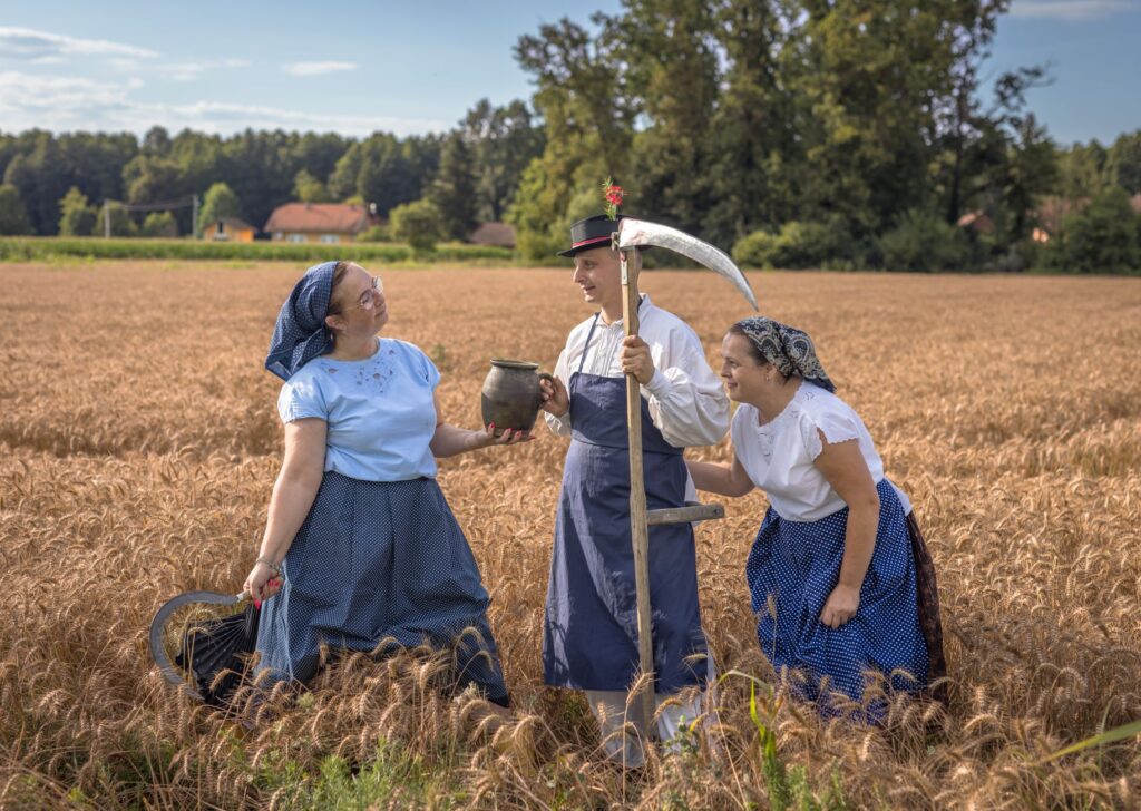 Three adults in vintage attire celebrate a traditional harvest in a wheat field under a bright sky. — skutki wichury w parku